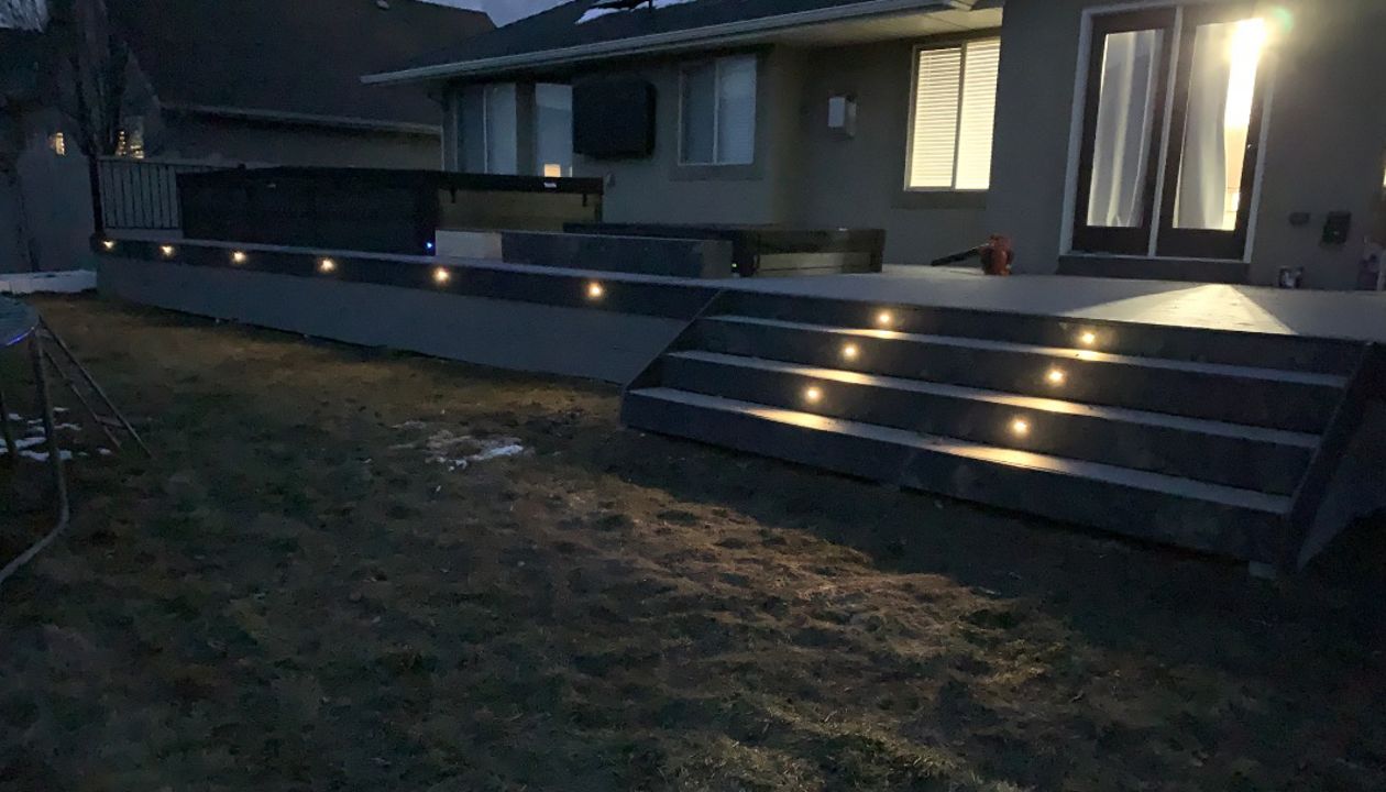 A custom deck designed to surround a swim spa and hot tub, complete with stairs and built-in lighting for safety and ambiance—perfect for relaxing day or night.