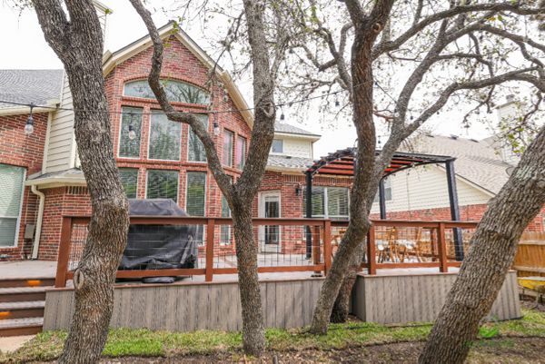 Raised Trex deck with skirting, wire railing and pergola behind a two-story brick home