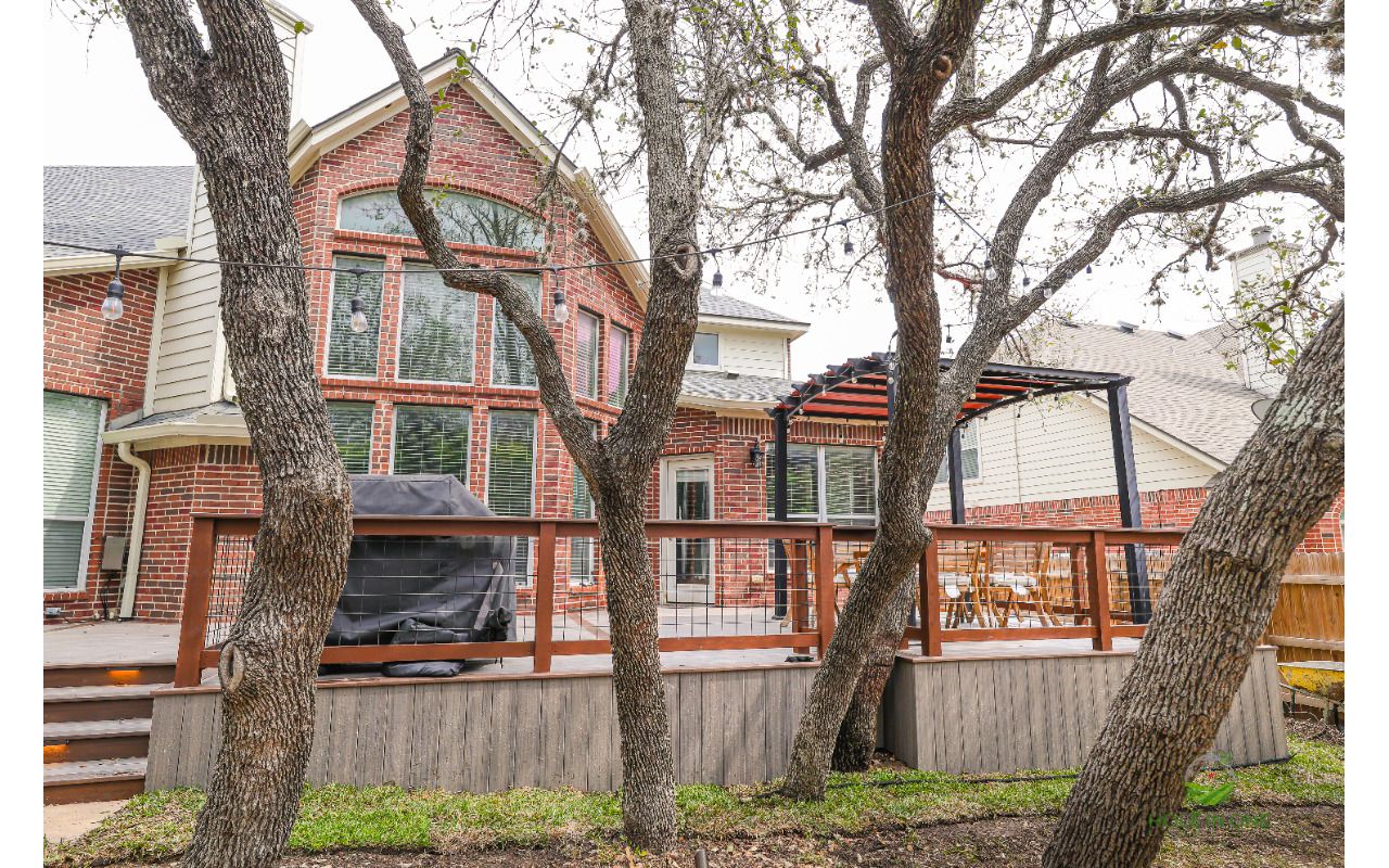 Raised Trex deck with skirting, wire railing and pergola behind a two-story brick home