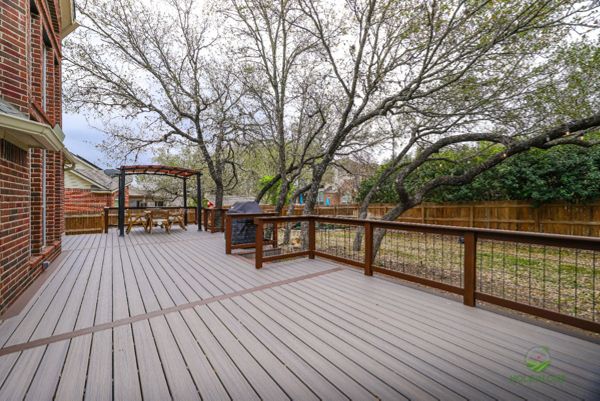 Large Trex deck under mature oaks with wood-and-wire railing and a pergola