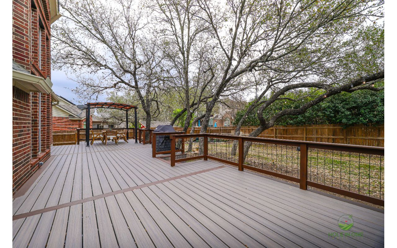 Large Trex deck under mature oaks with wood-and-wire railing and a pergola