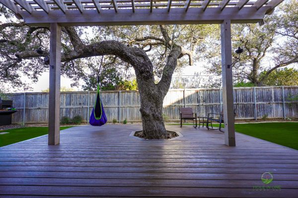 Trex composite deck built around a live oak with an open tree cutout, under a pergola in San Antonio