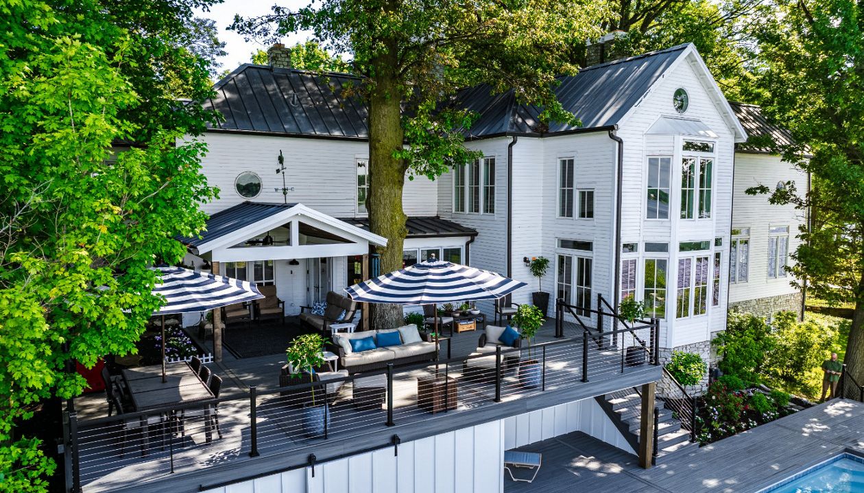 Elevated composite deck with cable railing and multiple seating areas designed for outdoor dining and relaxing beneath mature shade trees.