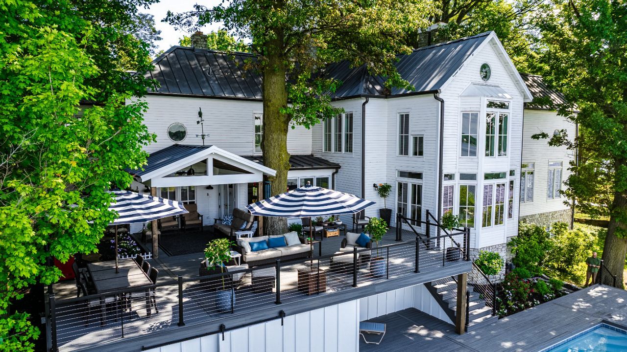 Elevated composite deck with cable railing and multiple seating areas designed for outdoor dining and relaxing beneath mature shade trees.