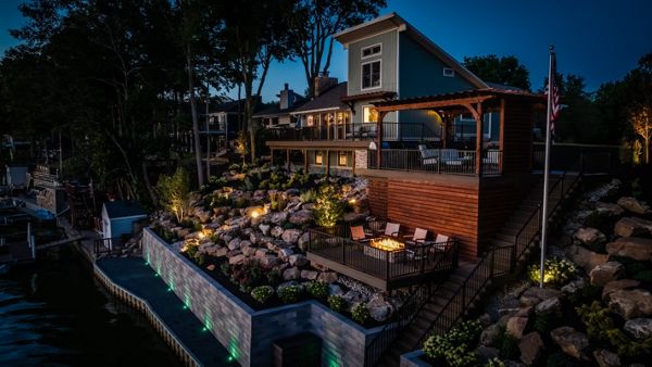 Lakeside composite deck with custom pergola, integrated fire pit lounge, and tiered landscape lighting overlooking the water.