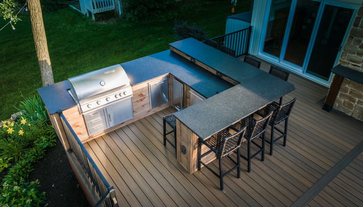 Custom outdoor kitchen built into a composite deck, featuring stainless steel grill components, stone countertops, and bar seating for outdoor entertaining.