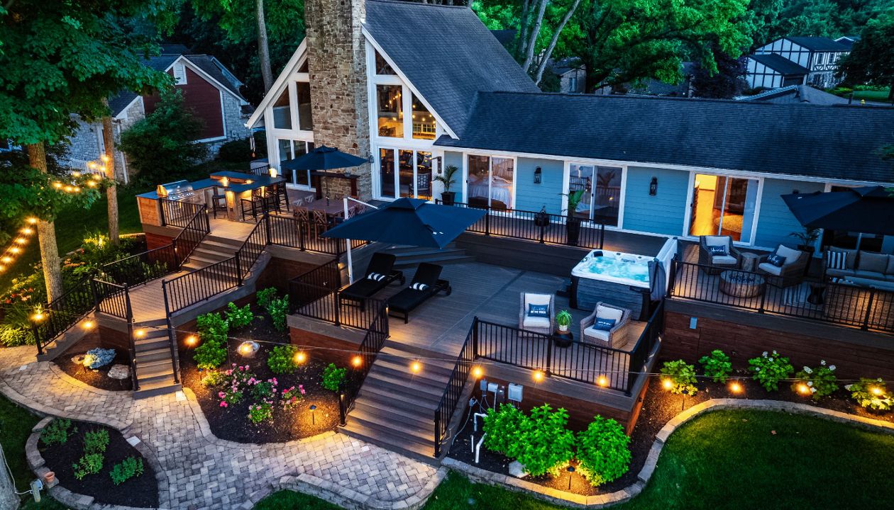 Multi-level Trex deck illuminated with landscape and ambient lighting, creating a dramatic nighttime outdoor living space.