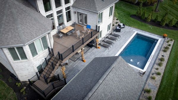 Second-story composite deck with aluminum railing overlooking a spacious pool patio and outdoor entertaining area.