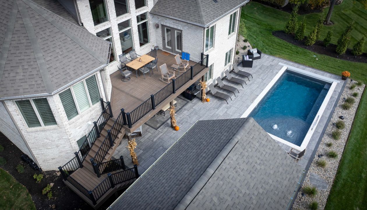 Second-story composite deck with aluminum railing overlooking a spacious pool patio and outdoor entertaining area.