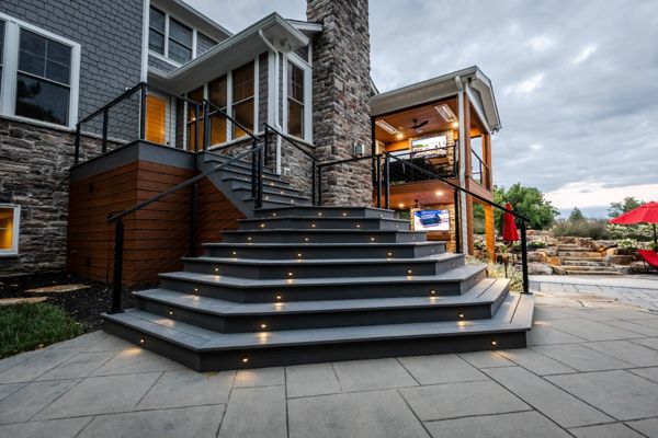 Wide composite deck staircase with integrated lighting leading to a lower-level patio and covered outdoor living area.