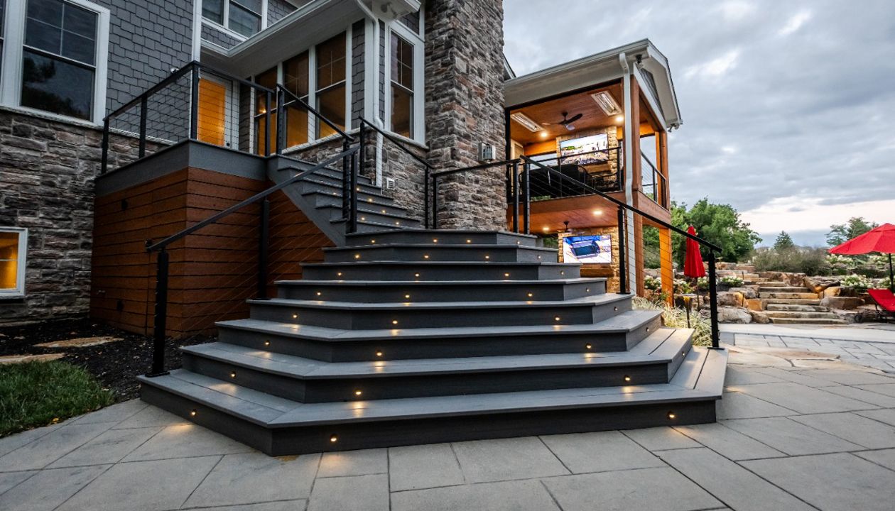 Wide composite deck staircase with integrated lighting leading to a lower-level patio and covered outdoor living area.