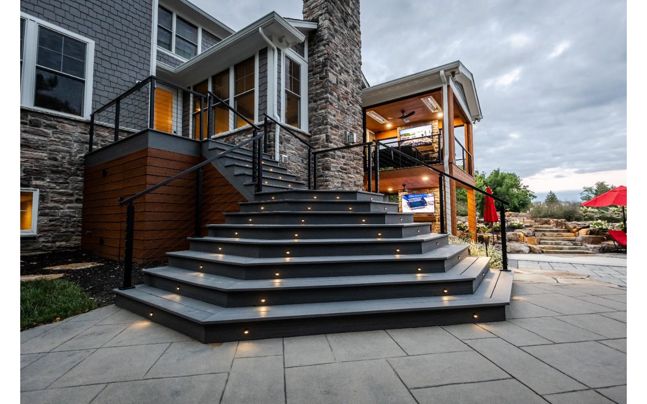 Wide composite deck staircase with integrated lighting leading to a lower-level patio and covered outdoor living area.