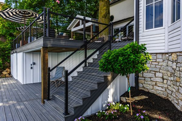 Elevated Trex deck with modern cable railing system and custom staircase connecting the upper deck to the backyard.