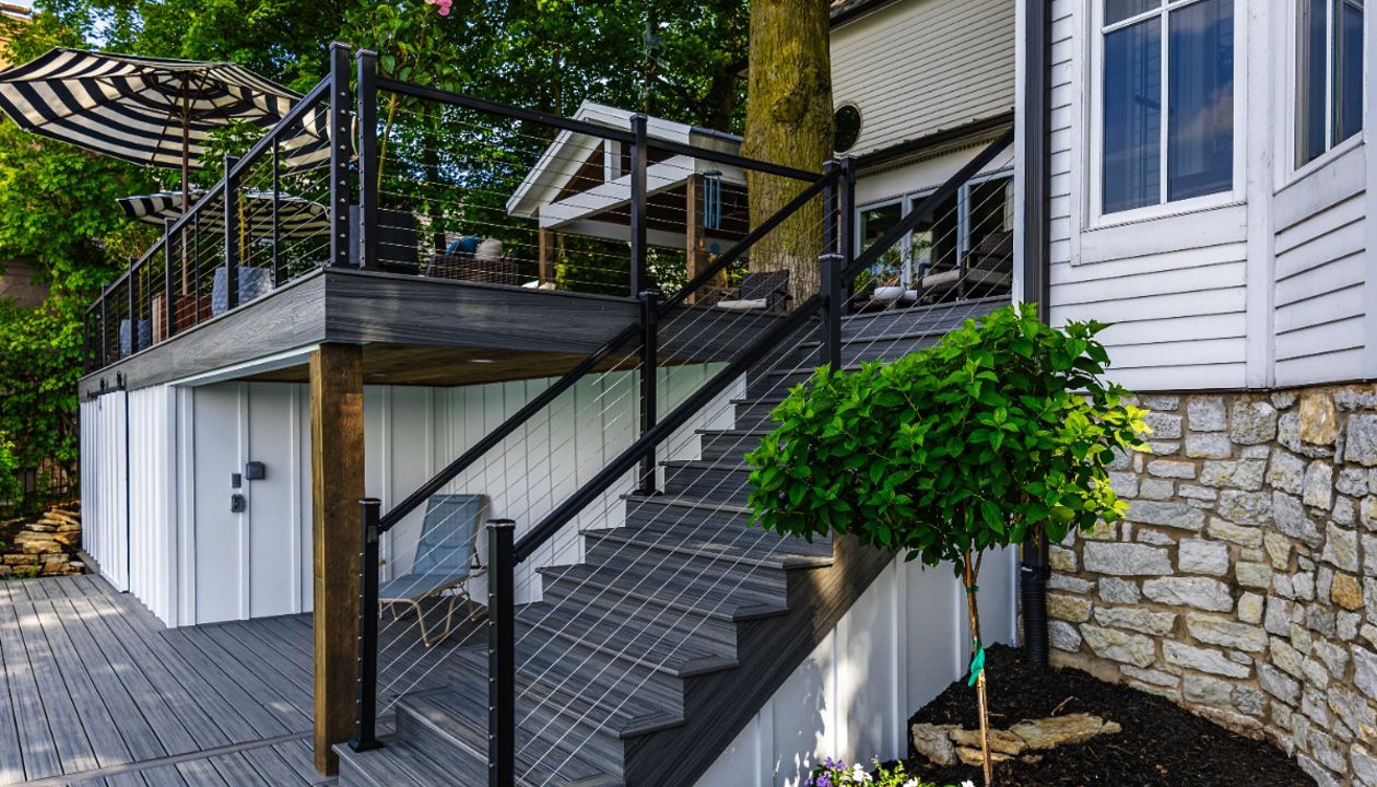 Elevated Trex deck with modern cable railing system and custom staircase connecting the upper deck to the backyard.