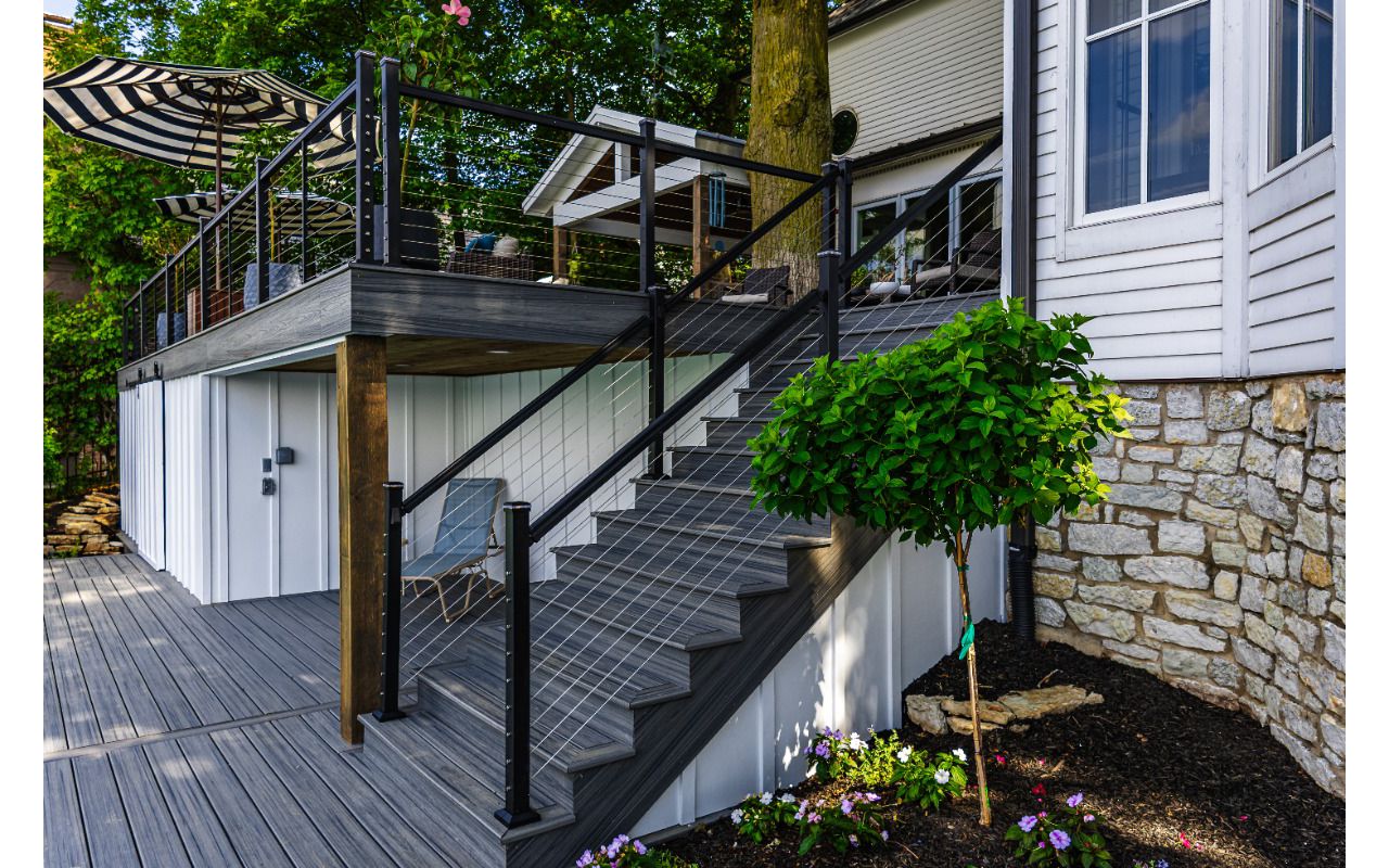Elevated Trex deck with modern cable railing system and custom staircase connecting the upper deck to the backyard.