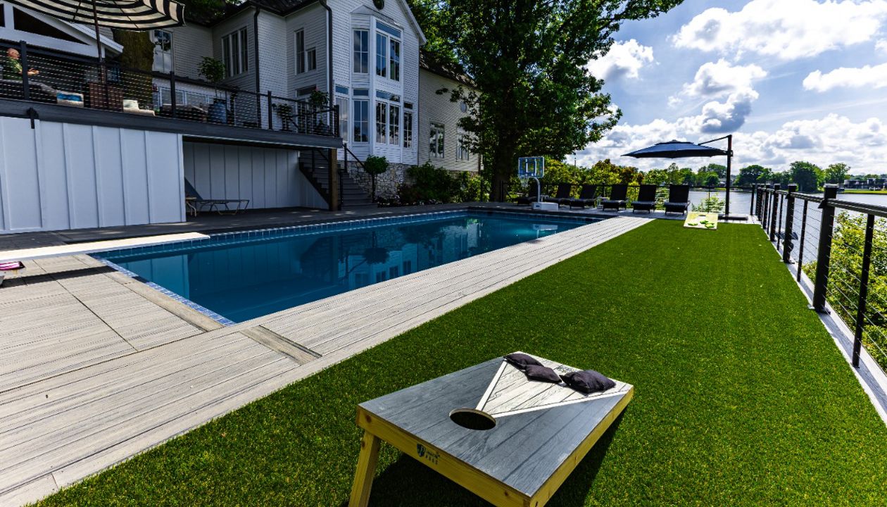 Large poolside Trex deck featuring integrated turf area for recreation, modern railing, and unobstructed lakefront views.