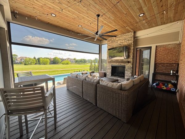 Covered composite deck with fireplace, TV, ceiling fan, and retractable screens creating a comfortable outdoor living room.