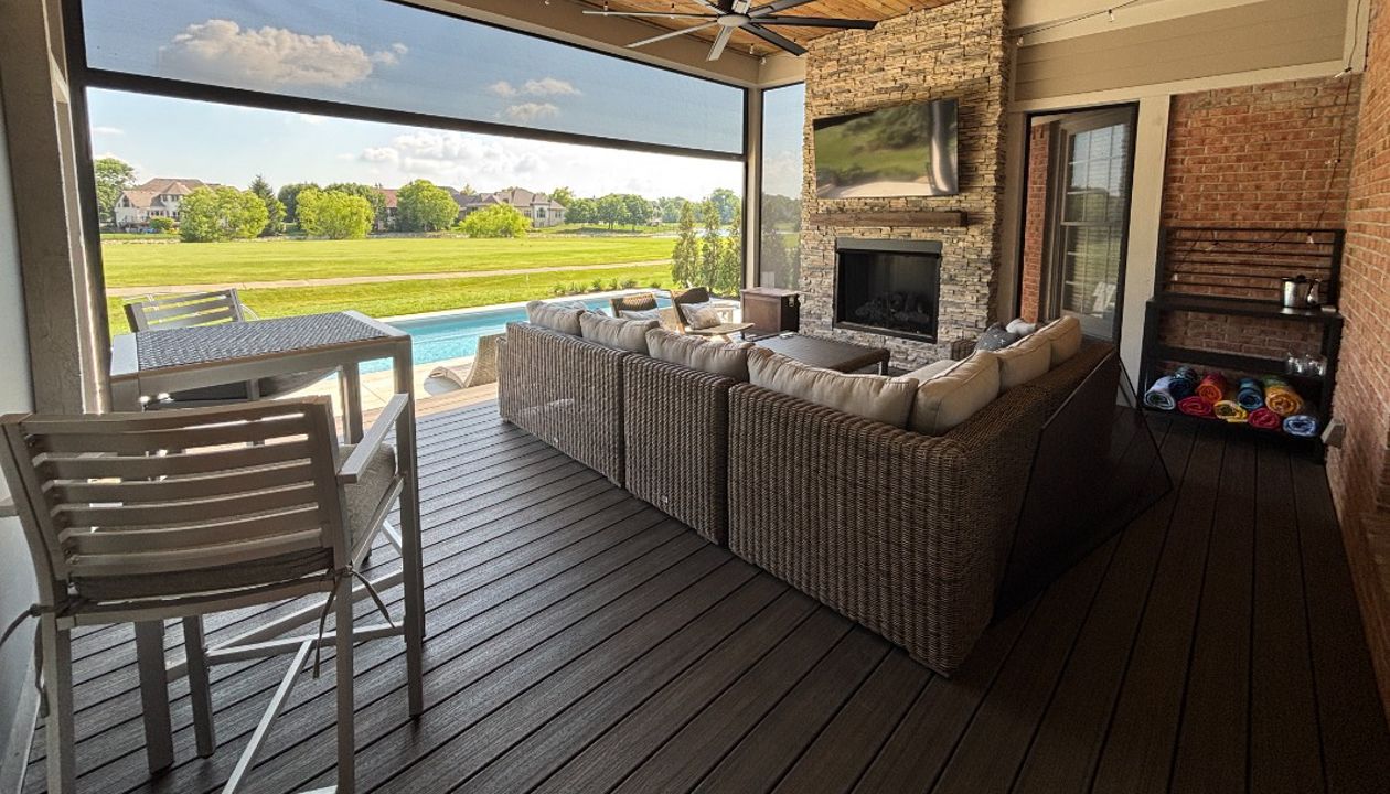 Covered composite deck with fireplace, TV, ceiling fan, and retractable screens creating a comfortable outdoor living room.