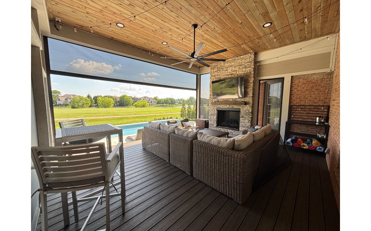 Covered composite deck with fireplace, TV, ceiling fan, and retractable screens creating a comfortable outdoor living room.