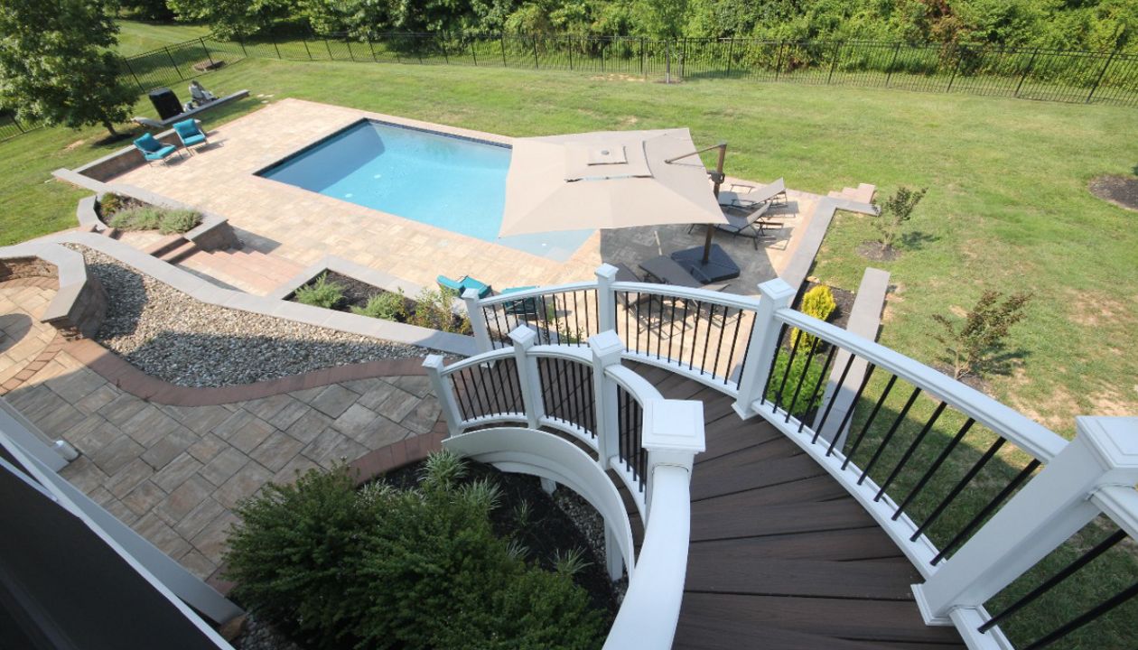 Curved deck steps down to tiered patio and pool area Highland, MD
