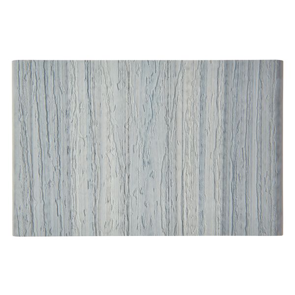 The image shows a rectangular object featuring a light blue and gray wood grain texture. The surface appears flat and smooth, resembling a wooden panel or decorative board. The vertical grain lines create a natural, organic pattern, and the overall palette is cool and muted. No visible text, numbers, or logos are present.