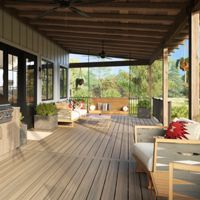 A large covered porch features a built-in outdoor kitchen with a stainless steel grill and sink, complemented by wooden cabinetry. Comfortable seating areas with cushioned chairs and decorative pillows are arranged along the deck, creating a welcoming space for relaxation or entertaining. The setting is bright and airy, with natural wood tones and views of greenery in the background. Ceiling fans and open shelving add functional and decorative touches.