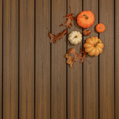 A small group of assorted pumpkins and dried autumn leaves are arranged on the upper right corner of a brown wooden plank surface. The pumpkins vary in size and color, including orange and white varieties. The setting evokes a fall or harvest theme with a natural, rustic background. No visible text or numbers are present in the image.