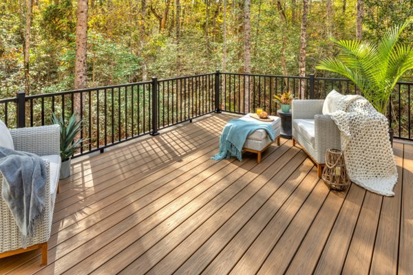 A Trex deck in the color Toasted Sand in a woodsy backyard with attractive deck furniture and plants dressing the deck, and lined with Trex Signature railing.