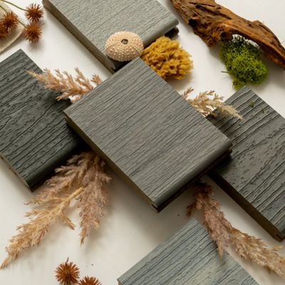 A collection of textured wood samples arranged with natural elements like dried flowers, moss, driftwood, and coral. The setting emphasizes earthy tones and organic aesthetics. The wood samples feature varied grain patterns and shades, creating a harmonious visual composition.