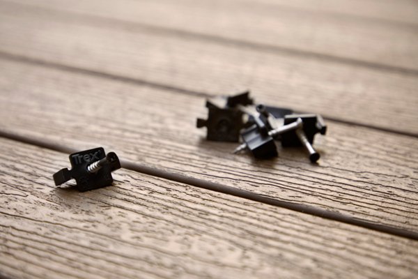 Trex hidden fasteners resting on a Trex deck with one in focus while the rest are on a pile inn the back.