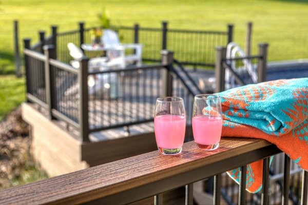 Two drinks and towels laid on a railing by an above-ground pool