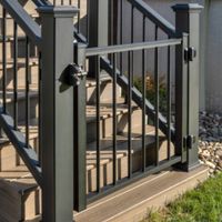 A sturdy black metal gate installed at the base of a wooden staircase, surrounded by a landscaped yard with grass and decorative stones. The gate features vertical bars and secure locking mechanisms, providing safety and functionality. The setting includes a residential outdoor area with nearby buildings visible in the background.