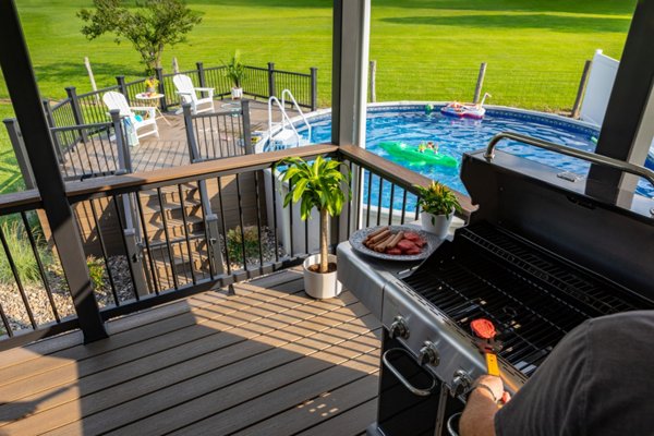 Backyard dad barbequing hamburgers and hotdogs on a Trex deck with an above ground pool in the background.