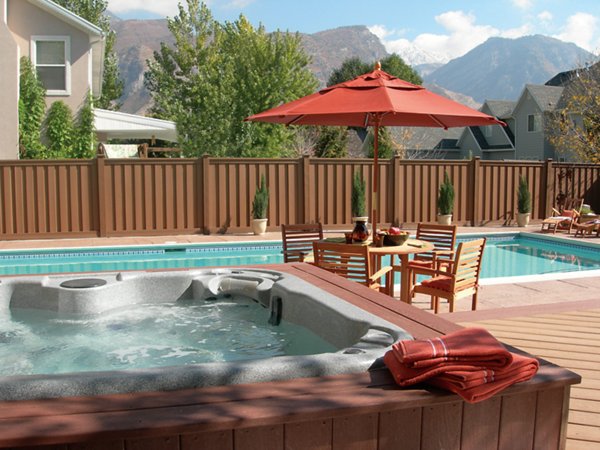 Fenced in yard with a pool and hot tub and outdoor dining table with an umbrella. 