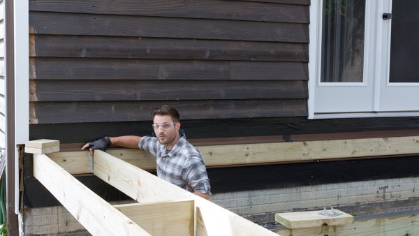 person sliding joist hanger from bottom of joist for proper installation