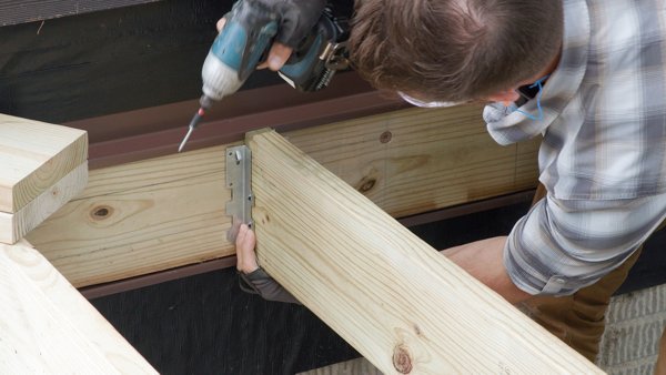 person fastening joist hanger to ledger board