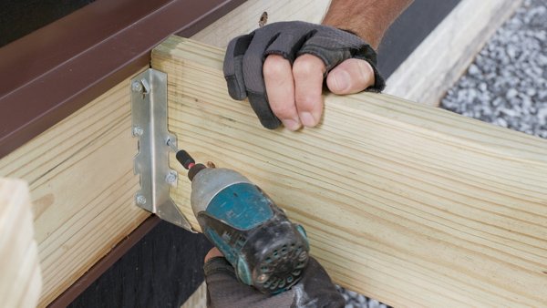person screwing angle holes of joist hanger into the ledger board