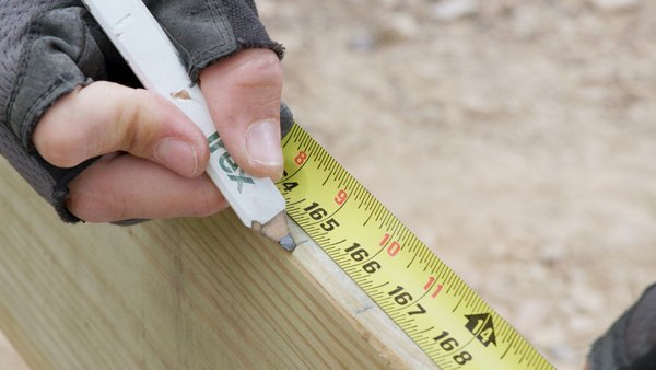 using a tape measure to mark the deck end length on the outside rim joist