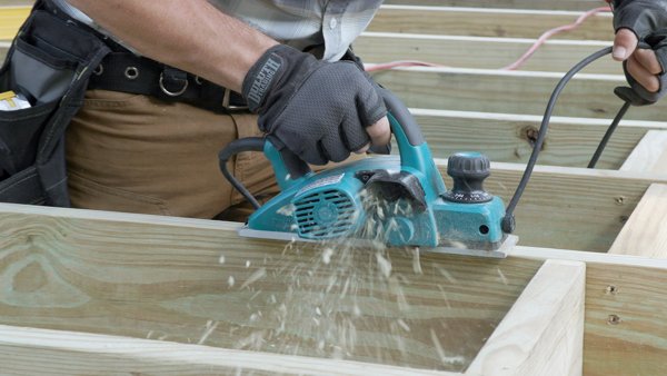 person using an electric hand planer to cut high spots of joist