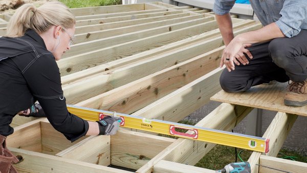 A woman and man working to install a deck and making sure it is level with a tool. 