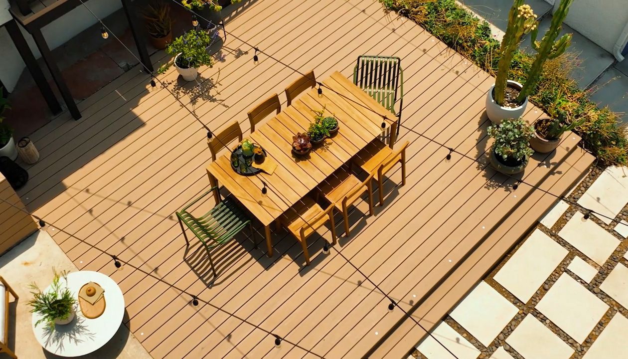 A beautiful backyard deck in the color Carmel exposed to bright sun. The deck is decorated with desert plants and an attractive outdoor dining table set.