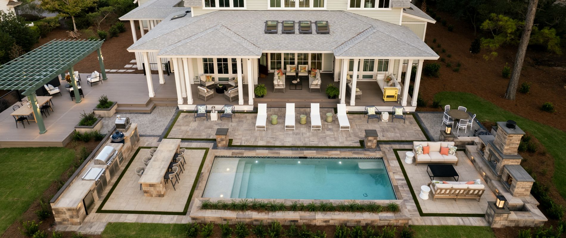 A above the home view of the backyard where you can see the pool deck, deck, dining, and outdoor kitchen space. 