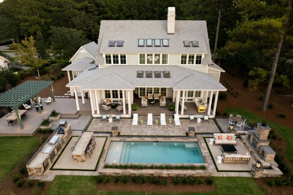 HGTV Dream Home 2025 aerial photo of the backyard which features Trex decking, railing, lighting, and pergola. The backyard also features a beautiful pool, outdoor kitchen, and many nice seating and dining areas. 