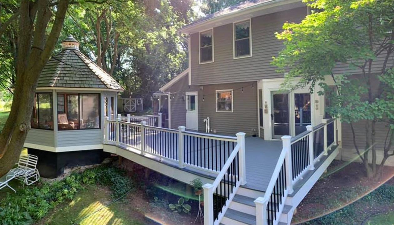 This deck features white transcend railing with black square aluminum balusters. It consists of Trex select pebble grey as the main decking and Trex transcend island mist as the picture frame, middle divider, and drink rail.