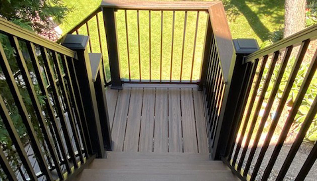 Trex/Transcend/Spiced Rum/Composite Decking with Trex/Signature/Aluminum Railing (black) between Trex/Composite Post Sleeves (black) and Trex/Transcend/Spiced Rum/Composite Decking/Drink Rail