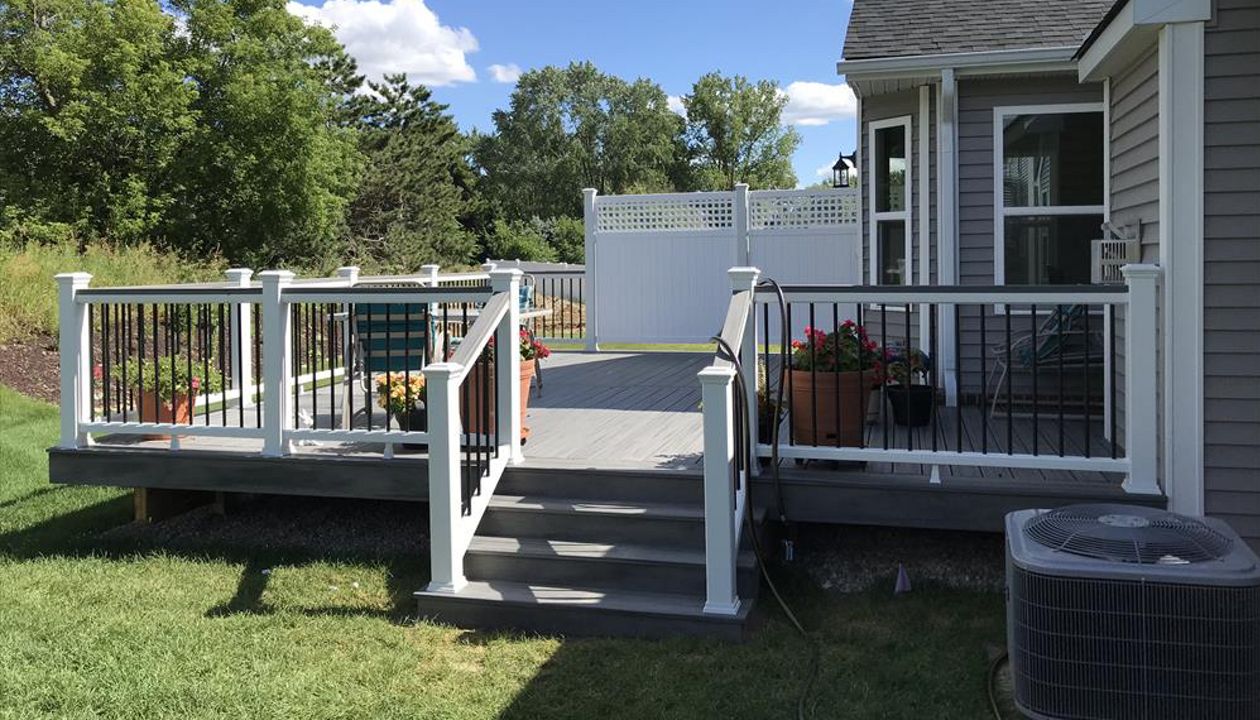 Deck in New Hudson, MI., constructed out of Trex Transcend Tropical decking in Island Mist and complimented by Classic White Trex railing with black balusters and Classic White privacy wall.