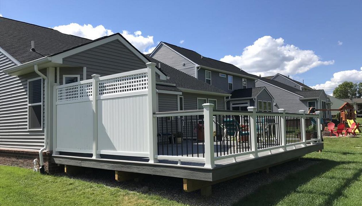 Deck in New Hudson, MI., constructed out of Trex Transcend Tropical decking in Island Mist and complimented by Classic White Trex railing with black balusters and Classic White privacy wall.