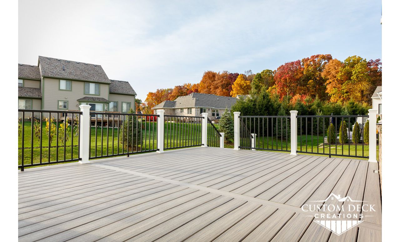 Trex Enhance Naturals Rocky Harbor decking with Trex Signature aluminum railing in black, with white composite Trex railing posts. Deck was wider than the longest decking board, so to avoid any unsightly butt joints a parting board was installed.