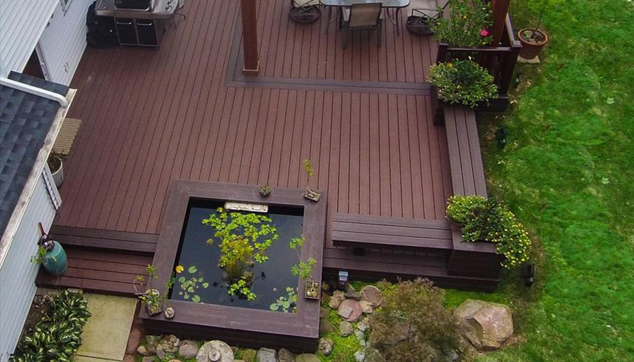 Ground level Asian garden deck featuring Trex Transcend Fire Pit decking, custom Vintage lantern boarder, Cedar Pergola, Koi pond, and Transcend Vintage Lantern railing.