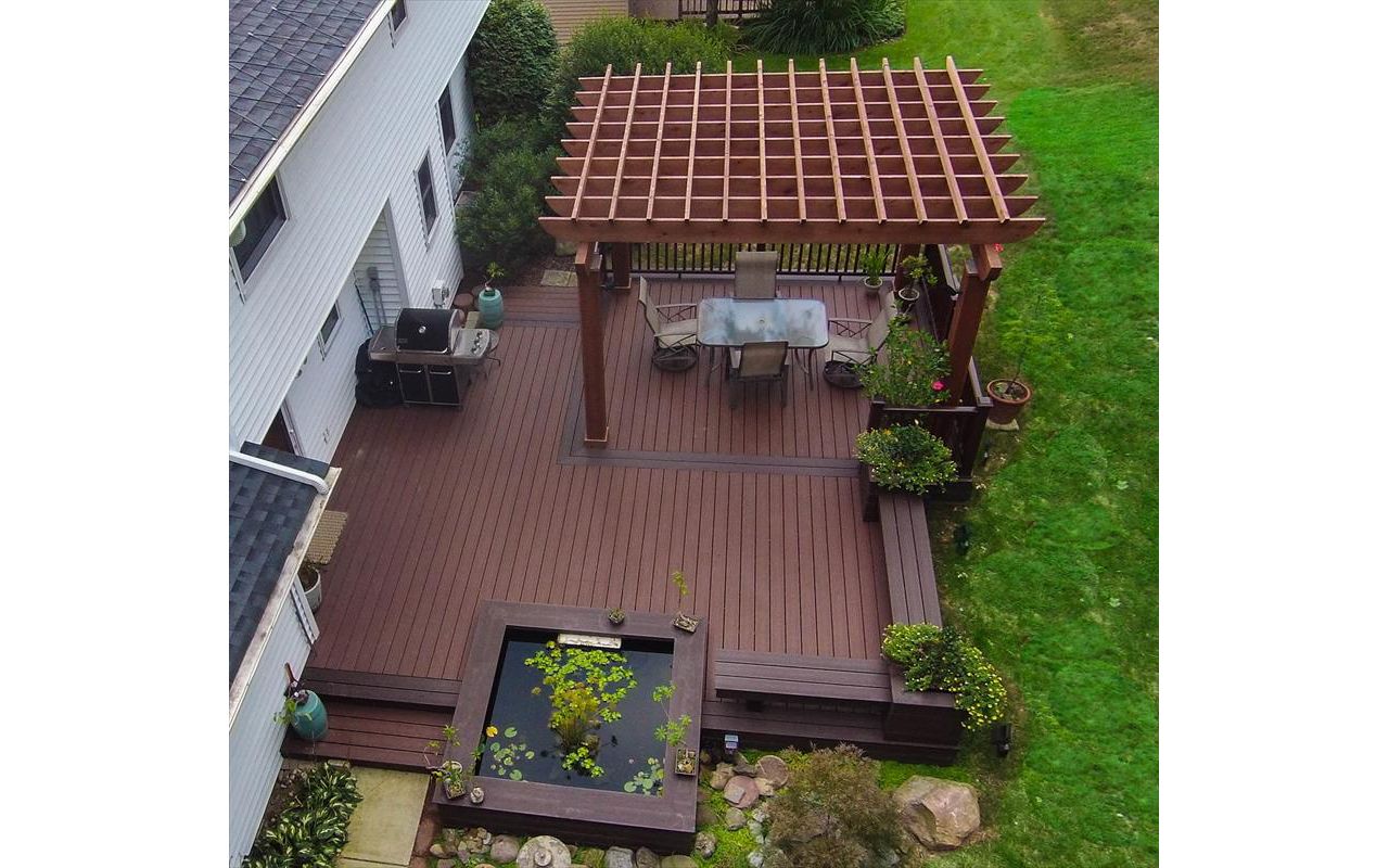Ground level Asian garden deck featuring Trex Transcend Fire Pit decking, custom Vintage lantern boarder, Cedar Pergola, Koi pond, and Transcend Vintage Lantern railing.